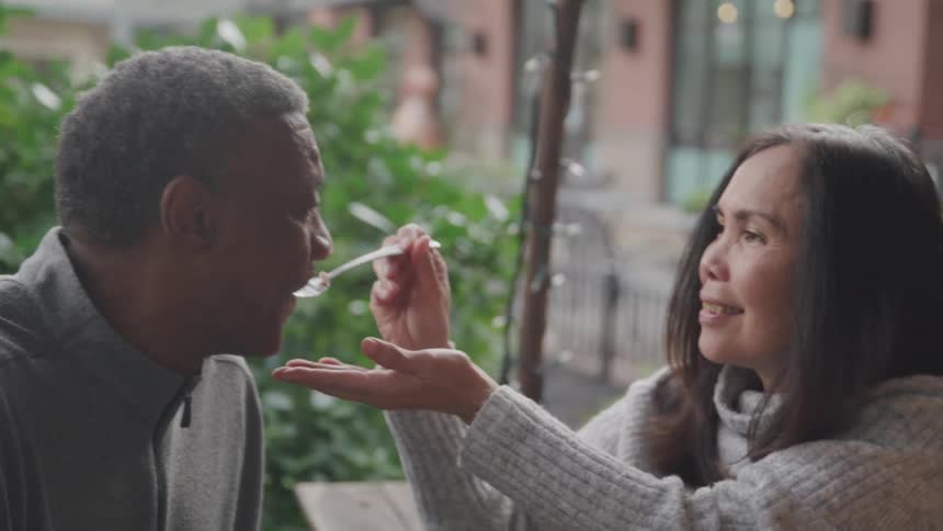 Woman gives man a bite of food from her fork at a cafe