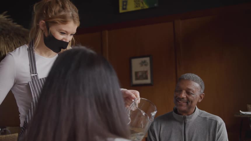 Waitress pours water for two diners sitting in a cafe