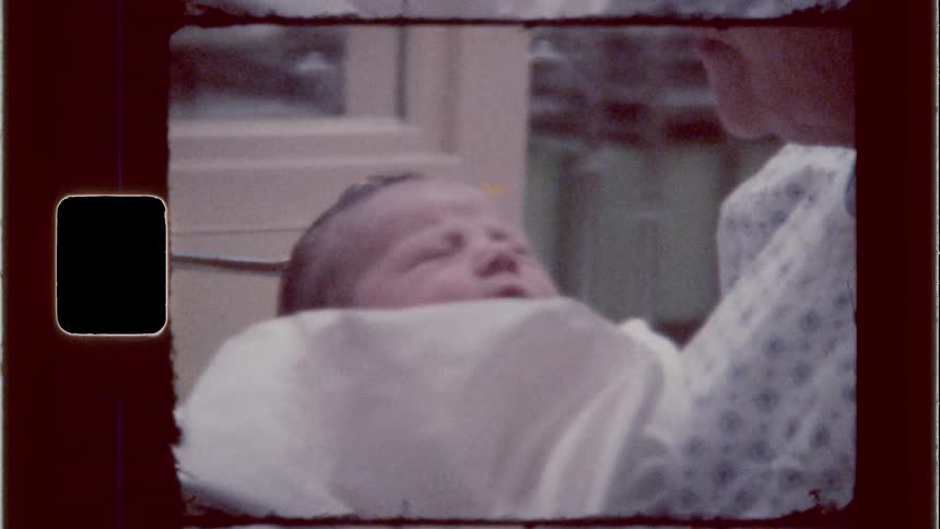 A newborn baby is being held swaddled by a nurse