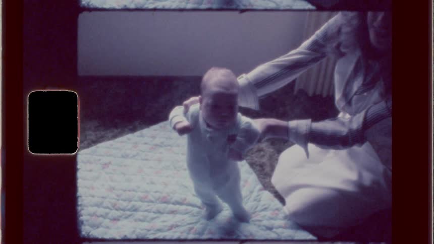 A mother lifts her baby up and helps him stand
