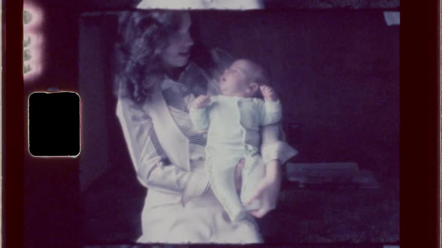 A woman with voluminous hair holding a baby in a dimly lit room
