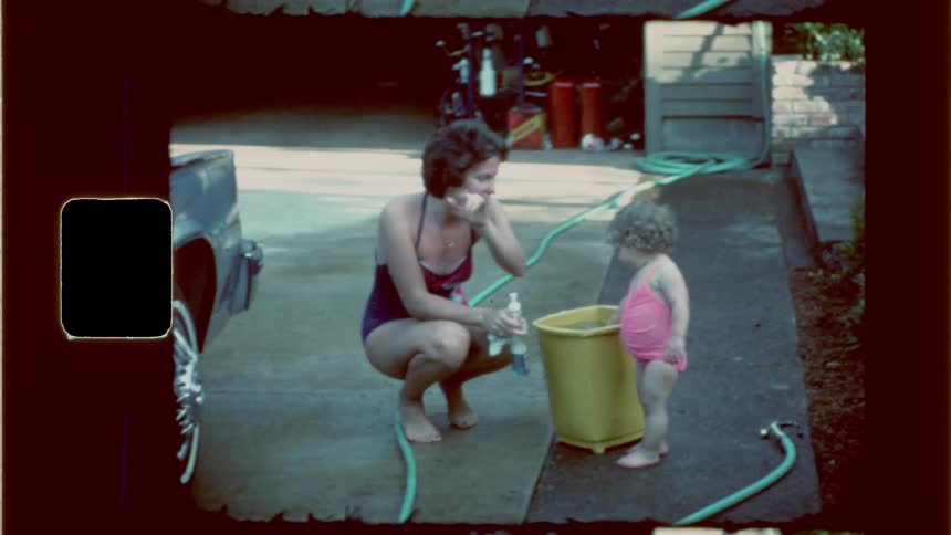 Grandmother and baby standing near a bucket full of water ready to wash the car in the driveway