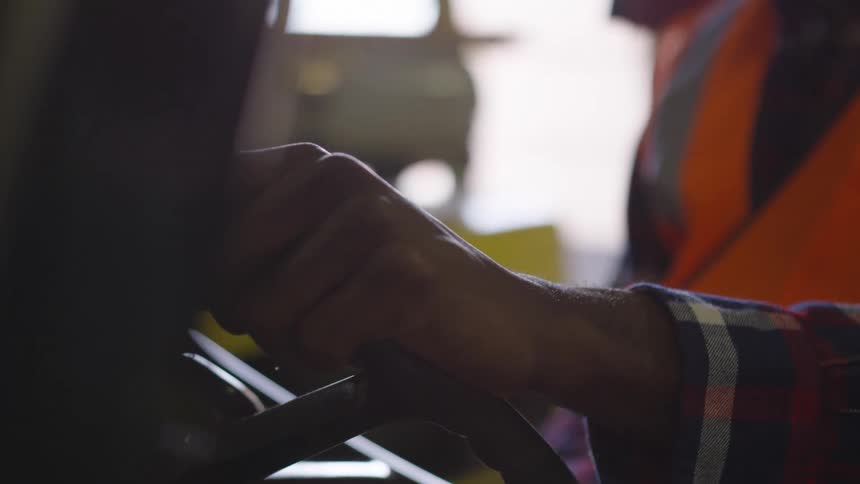 Man sitting in a forklift grips the steering wheel with one hand