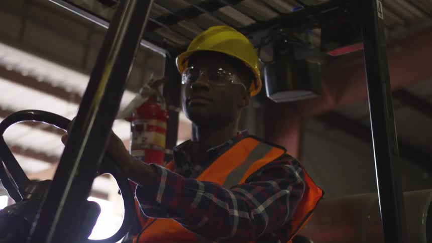 A worker is sitting on a forklift in a lumberyard