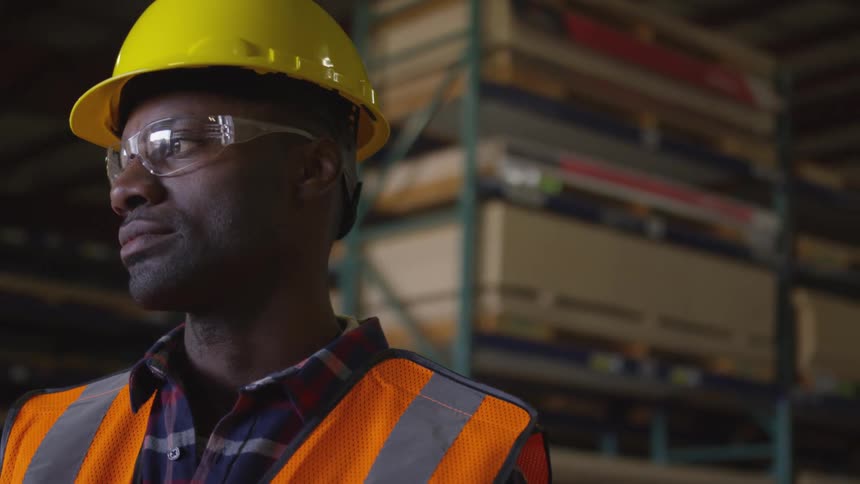 A worker wearing safety gear is standing in a lumber yard