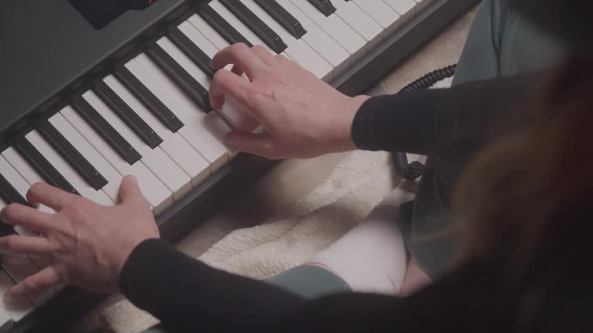 A woman wearing a black sweater and jeans plays an electric keyboard while sitting on the floor