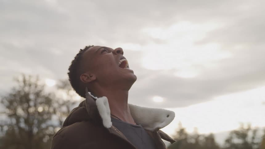The black man is standing and looking up at the sky and yelling