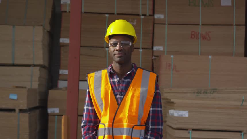 Man in a hard hat and safety vest standing in front of bundles of flat wood