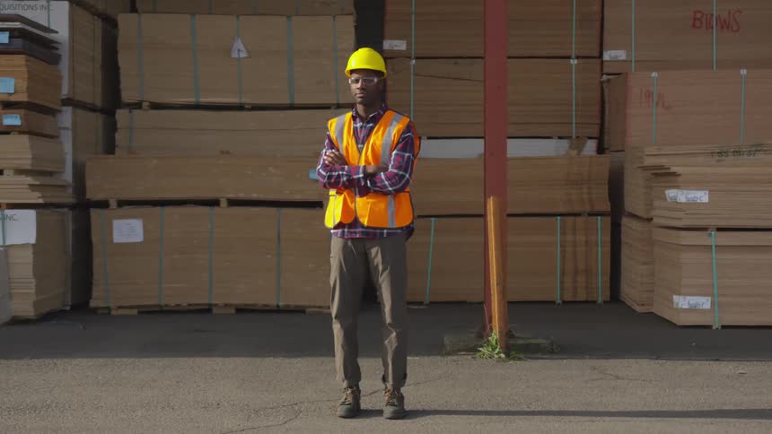 The employee is standing in front of the stacks of lumber