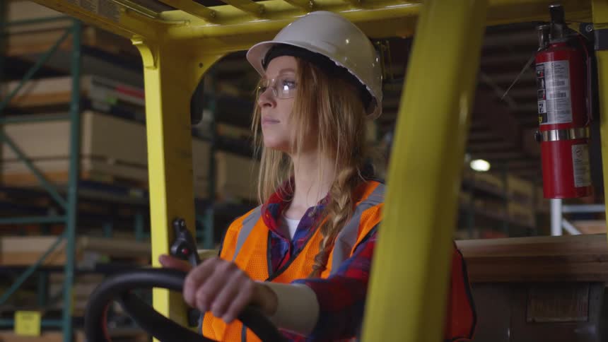 Woman sitting in a forklift holds the steering wheel with only one hand