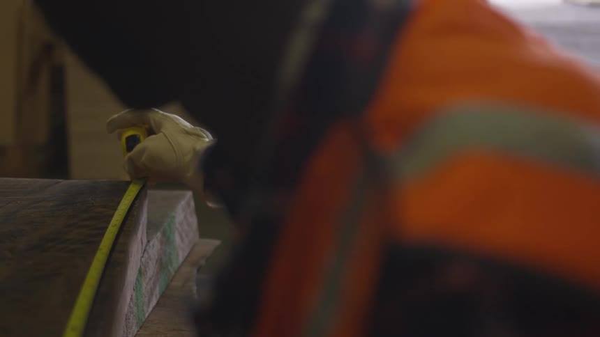 Man uses a measuring tape on a thick piece of wood