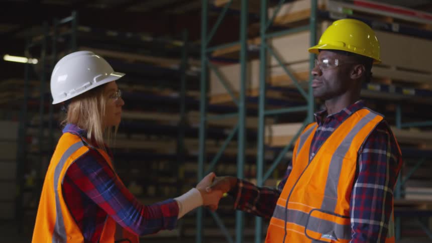 Man and woman in hard hats shake hands in front of plywood