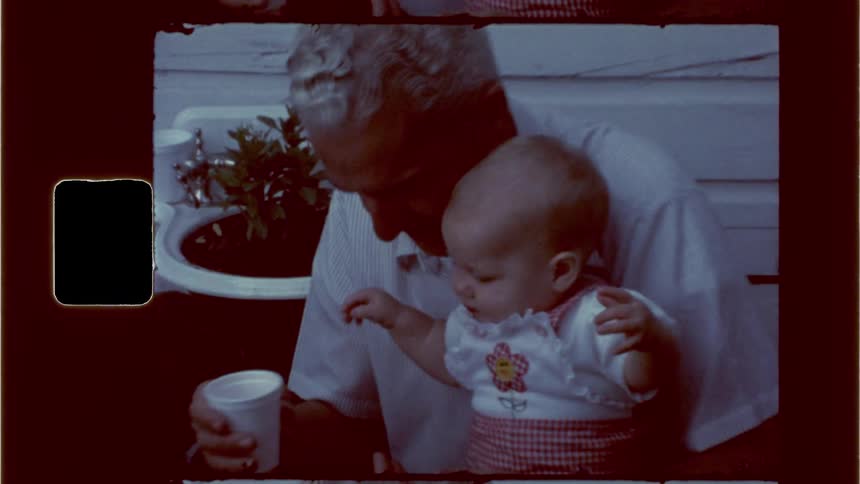 Grandfather gives his granddaughter a sip from a cup while his grandson plays on a bench nearby