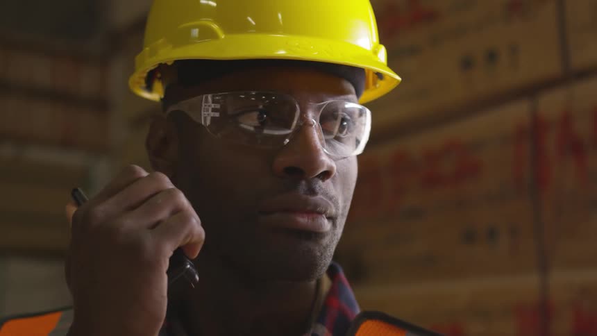 Man in a hard hat observes something and speaks into a walkie talkie