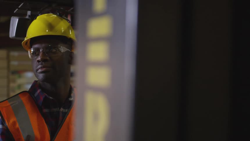 A man with an orange vest sits in a shipping warehouse inside a tiny shipping car