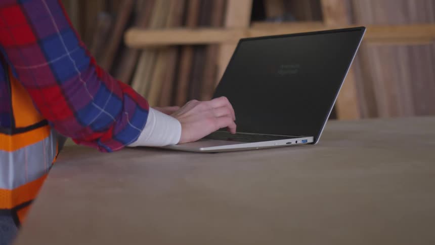 Person typing on a laptop with lumber stacked in front of them