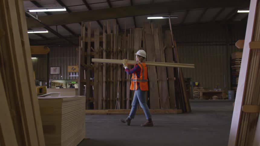 Woman carries lumber through a warehouse
