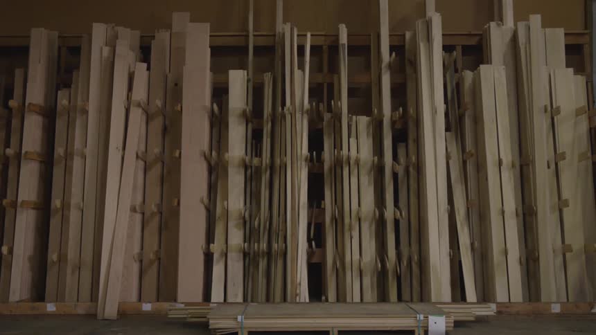 Multiple wooden boards stand upright in a storage area neatly organized on shelves
