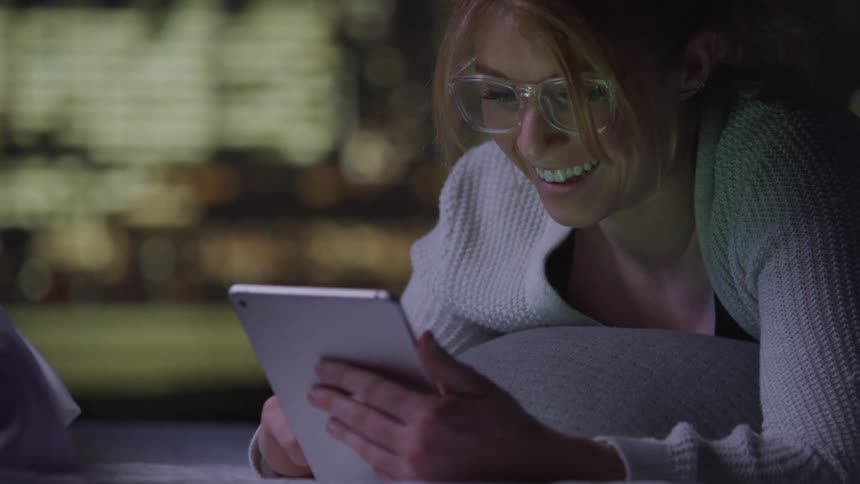 A smiling woman holds a tablet and waves a greeting to a person on a video call