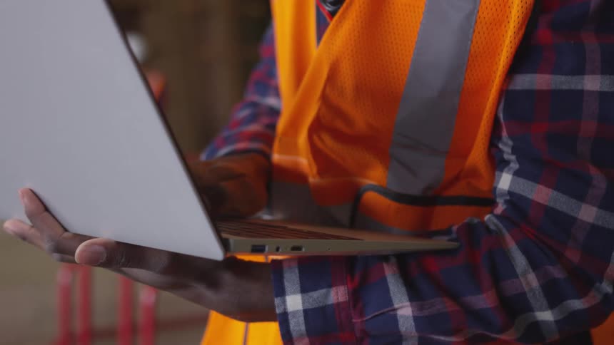 A man wearing a safety vest is holding a laptop