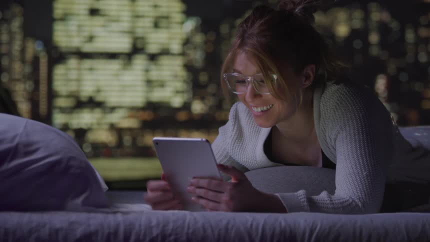 A woman laughs and smiles while using her tablet