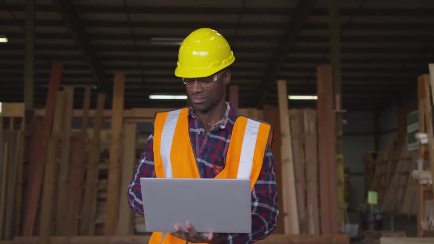 Man looks around a warehouse before typing onto a laptop computer
