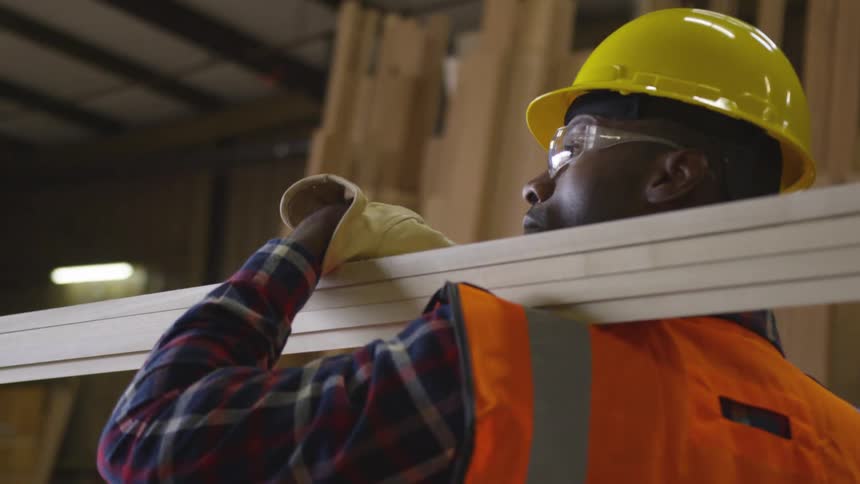 Man carries lumber on his shoulder with one hand