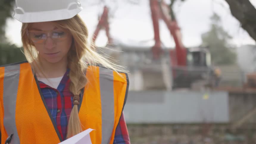 Woman examines a sheet of paper with plans at a construction site
