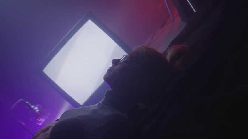 A woman is resting in front of the flashing television
