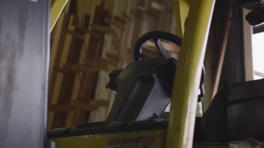 A yellow forklift sits empty in a warehouse filled with wood