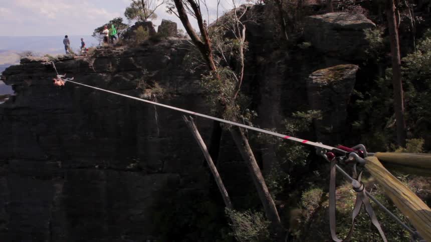 A person hangs from a tightrope in a canyon