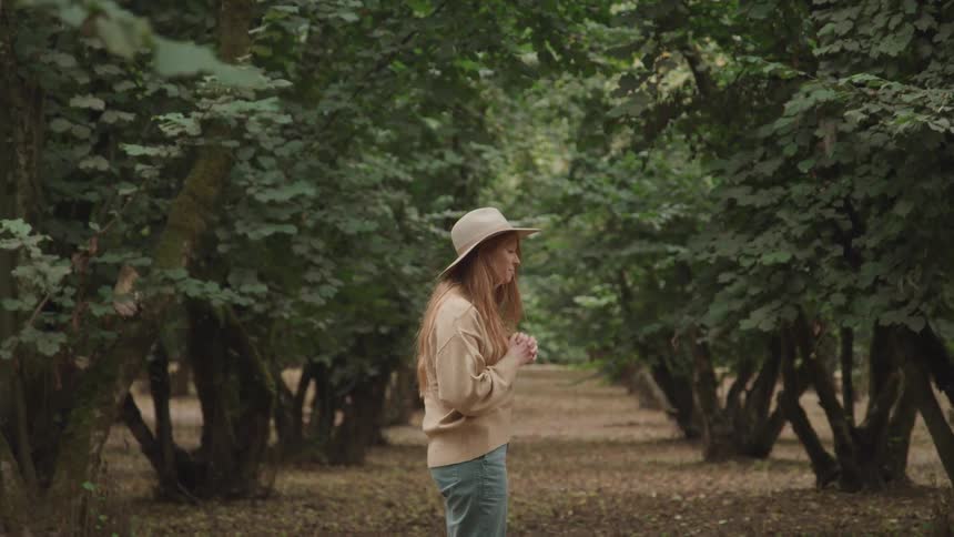 Woman standing in the middle of a grove prays and looks up to the sky