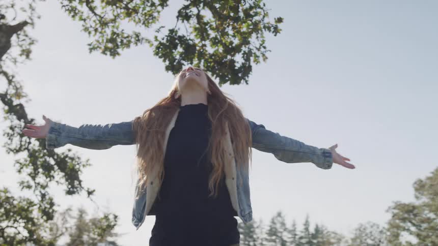 Woman spinning around with arms wide open under a large tree