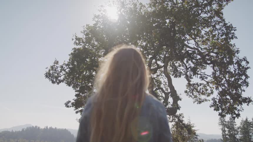 A woman is standing and staring at a tree in a forest