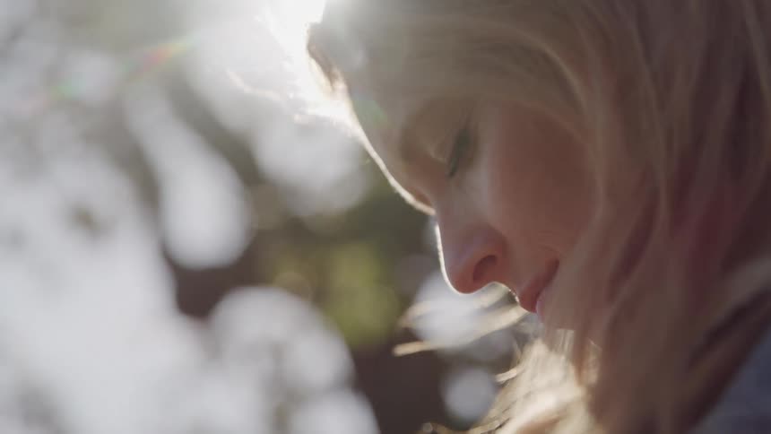 A side profile of a womans face with her head slightly bowed is bathed in soft bright sunlight creating a dreamy ethereal effect