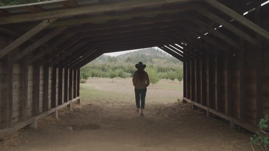 A woman is walking at a ranch and wearing a hat