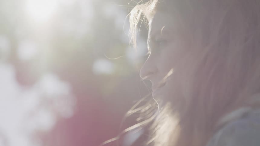 A woman with long light brown hair with sunlight filtering through the background creating a soft blurred effect