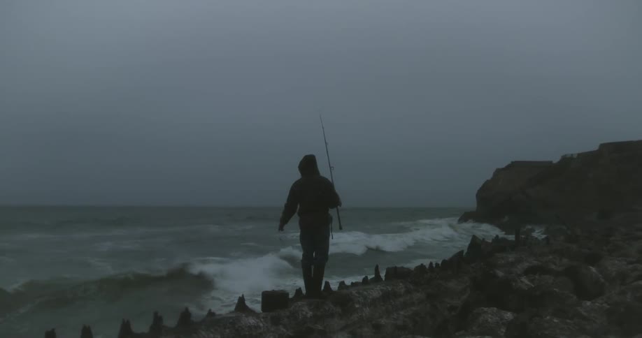 A fisherman fishes as waves crash ashore