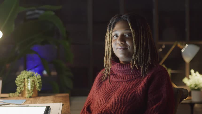 A black woman with locs turns her head toward the camera with a small smile