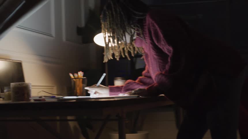 Woman leans over a table in a dimly lit room and writes