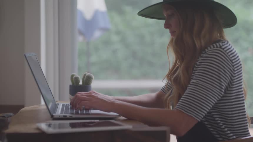 Teenage girl sitting at a desk near a window typing on a laptop computer