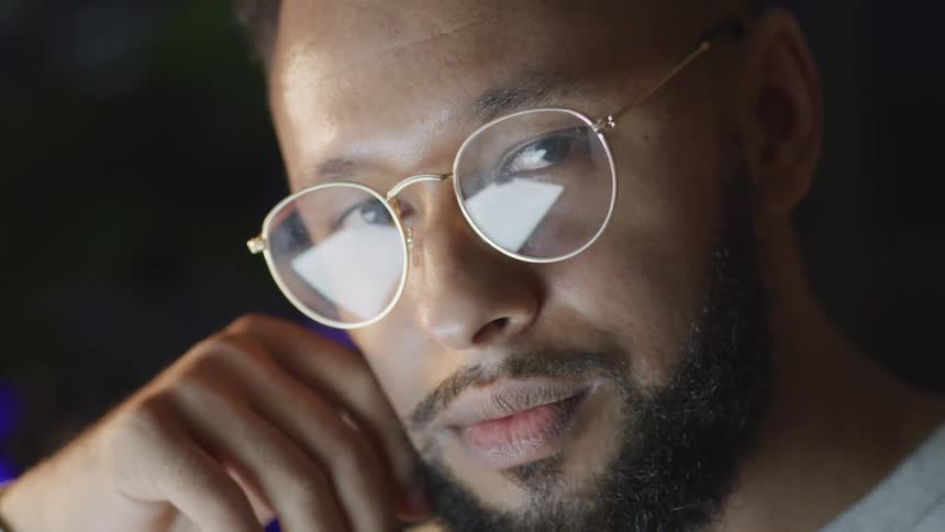 Man wearing glasses rests his face on the back of his hand and stares ahead