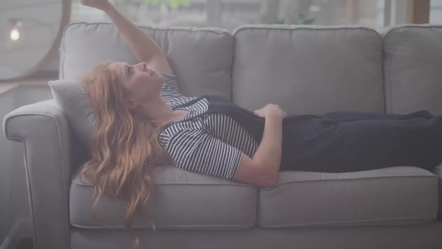 Woman sadly twirls her hair and rests her arm on her head while lying on the couch