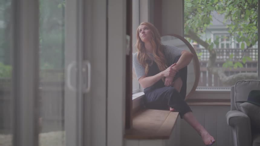 Woman sits on a window bench deep in thought