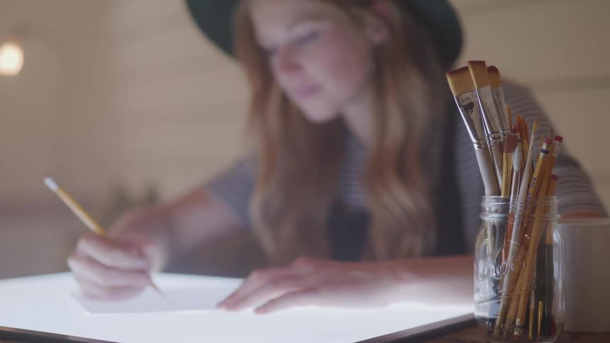 Closeup of brushes and a girl drawing on a sheet of paper
