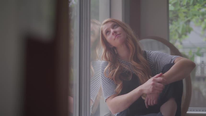 A woman is sitting and looking out the window