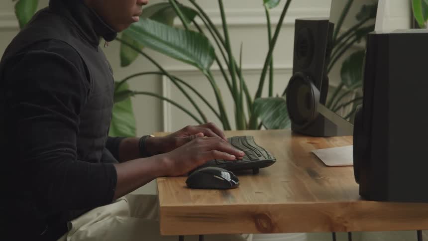 Man wearing headphones is sitting at a desk typing on a computer keyboard