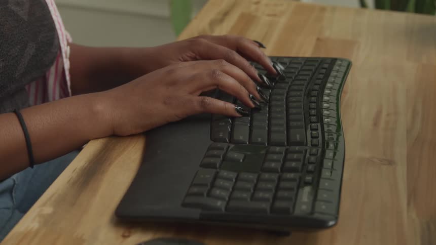 Woman with long painted fingernails types on a computer keyboard
