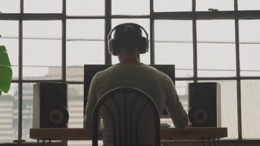 Guy from behind sitting at a desk with headphones listening to music