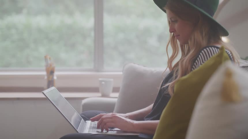 A woman is typing on her laptop while sitting on the couch